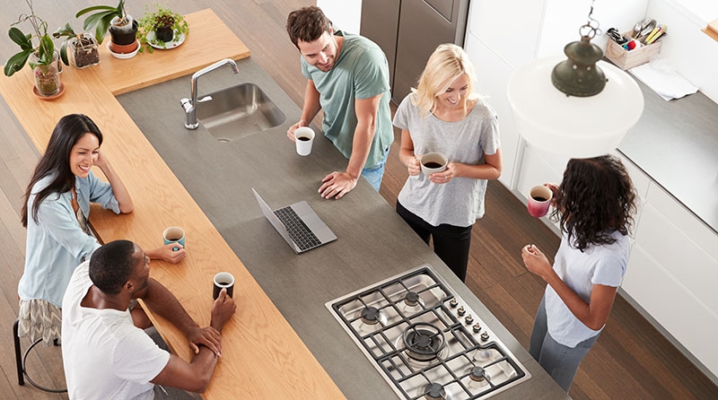 A group ofpeople sitting around a kitchen counter.