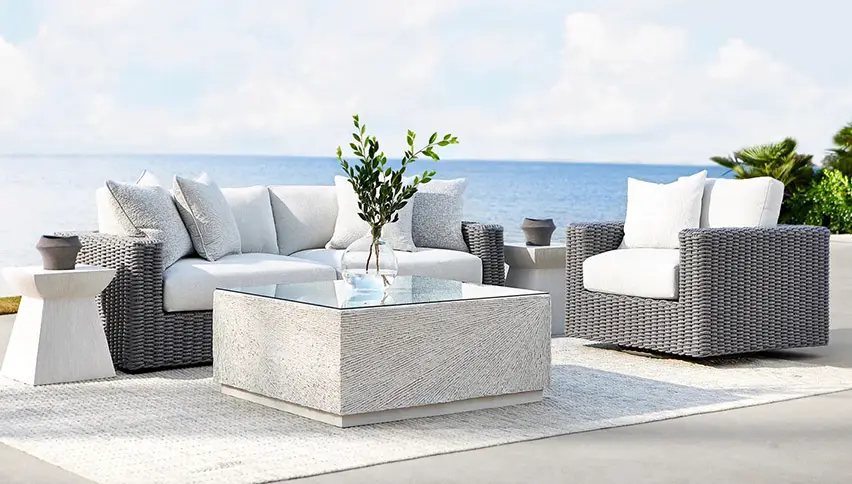 A wicker furniture set on a patio with a view of the ocean.