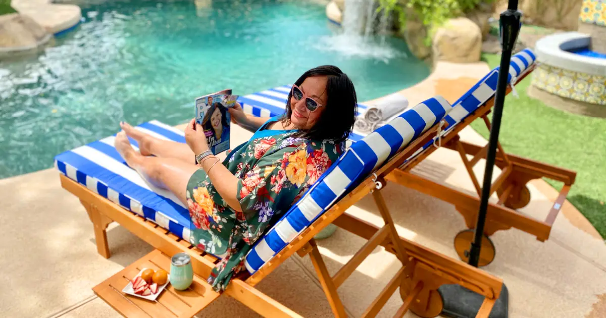 Woman relaxes in outdoor lounge chair near pool with magazine.