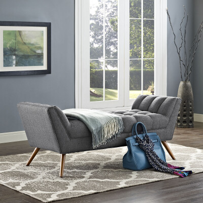 A gray upholstered bench in a room with a rug.