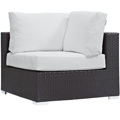 A wicker corner chair with white cushions.