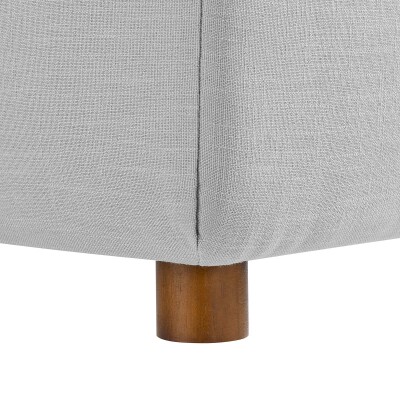 A close up of a grey fabric ottoman with wooden legs.