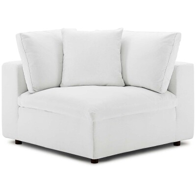 A white corner chair with pillows on it.